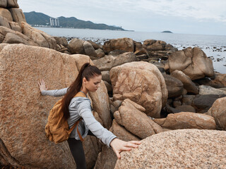 Young woman navigating rocky coastline, wearing casual outdoor clothing, showcasing determination...