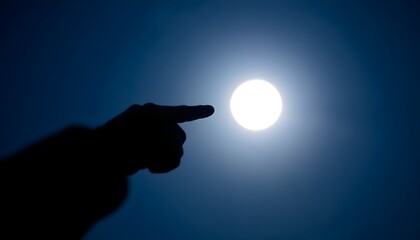 Hand pointing at a bright full moon in a clear blue sky, with a slight blur effect on the foreground. The scene conveys a sense of wonder and connection with the night sky.