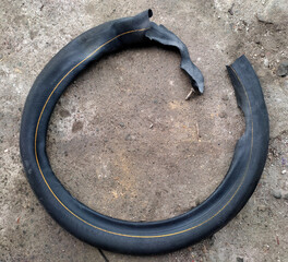 A torn motorcycle inner tube lying on the ground, damaged due to continuous use despite a puncture....