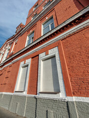 Fototapeta premium A historic facade with red bricks and two windows equipped with automatic white shutters. The photo showcases a blend of traditional design and modern security features.
