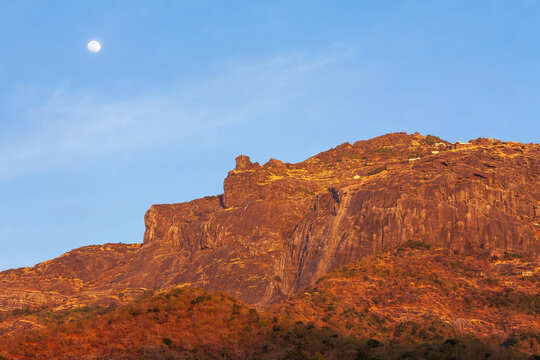 Scenic view of Girnar Hill at sunset with a clear blue sky and the moon rising, Junagadh, Gujarat, India.