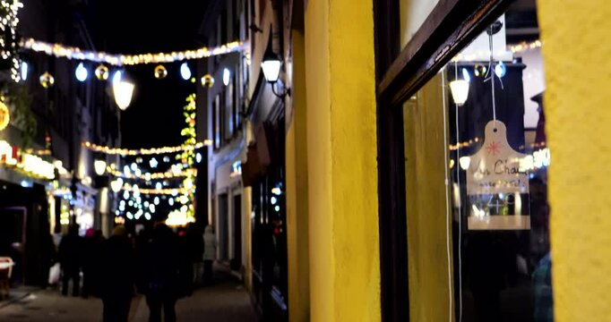 Bar window displaying vin chaud priced at 4 euros with silhouettes of people walking in a festive Strasbourg street adorned with lights.
