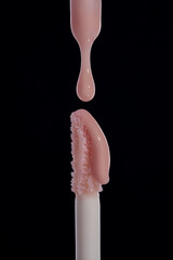 Drop of pink liquid lip gloss falls on applicator. Closeup shot on black background