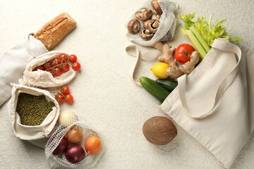 Eco bags with different food products on white textured table, flat lay. Space for text