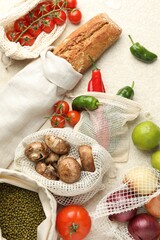 Eco bags with different food products on white textured table, flat lay
