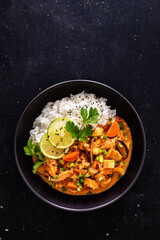Thai food - chicken nuggets with vegetables, mushrooms and rice in tomato and coconut milk sauce on black table