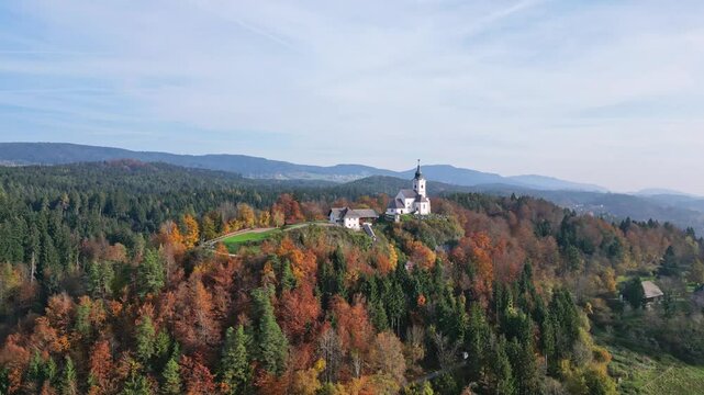 Aerial view of a picturesque chapel on a serene hill surrounded by autumn foliage and tranquil forest, Sternberg, Velden am Woerthersee, Carinthia, Austria.