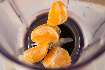 Tangerine pieces falling into blender to cook filling for pie on kitchen. Professional baker preparing ingredients for homemade pie. Culinary skills, cuisine, making dish meal. Domestic food recipe.