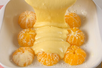 Cooking pouring cake batter over peeled mandarin oranges in baking dish. Professional pastry chef preparing tangerine pie, homemade citrus cake. Culinary, cuisine, food. Domestic recipe dessert.