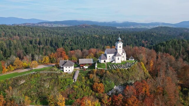Aerial view of a picturesque chapel on a hill surrounded by colorful autumn trees and serene forest, Sternberg, Velden am Woerthersee, Carinthia, Austria.