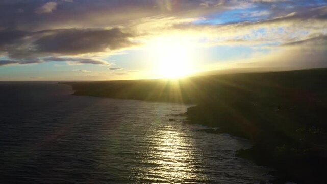 Aerial view of the Puna coastline at sunset, with golden sunlight reflecting on the ocean waves and rugged volcanic cliffs.