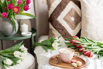 Cup with cappuccino and macarons, spring flowers tulips, morning concept, soy candle, woman's day, bedroom design