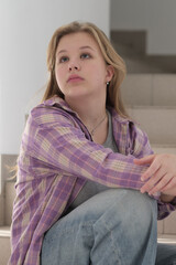 young woman sits thoughtfully on a staircase, her gaze directed into the distance. The image...