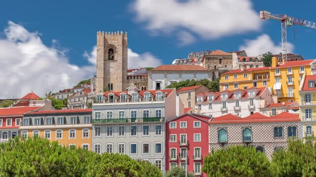 Square largo Jose Saramago timelapse hyperlapse at medieval quarter Alfama in Lisbon, sunny day with green trees and blue cloudy sky. Many colorful houses and Se de Lisboa cathedral on top. Portugal