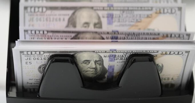 Money counting machine processes thick stack of dollar bills. Counting machine calculates total amount of dollar banknotes. Slow motion