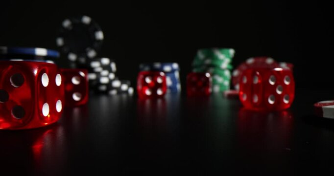 Collection of red gaming dices and poker chips rests on table. Colourful elements create atmosphere of excitement and unpredictability
