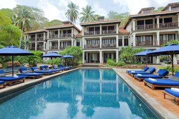 Blue Sun Loungers with Cushions and Umbrella by Poolside of Multi-Story Buildings in Phuket's Tropical Resort. Perfect for Hotel and Vacation Imagery.