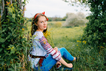 Woman in Traditional Embroidered Blouse Posing Outdoors Amid Greenery and Flowers
