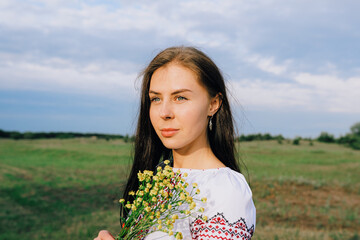 Woman in Traditional Embroidered Blouse Posing Outdoors Amid Greenery and Flowers