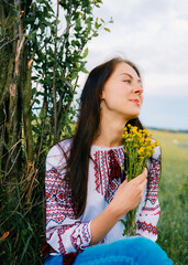 Woman in Traditional Embroidered Blouse Posing Outdoors Amid Greenery and Flowers