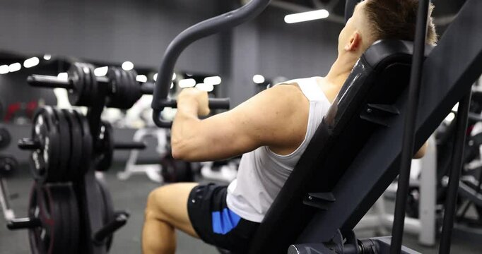Determined male athlete lifts weights on chest press machine in gym. Man focuses on building upper body strength and muscle mass in fitness center