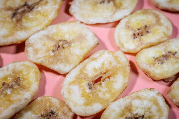 A close-up of freeze-dried banana chips arranged on a pink surface, highlighting their golden yellow color and crunchy texture. Perfect for food, snacks, and healthy eating themes.