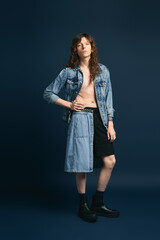 Handsome young man showcases trendy fashion in chic denim ensemble against a deep blue backdrop