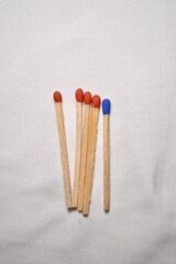 A single blue matchstick stands out among four red ones, arranged neatly on a plain white background.