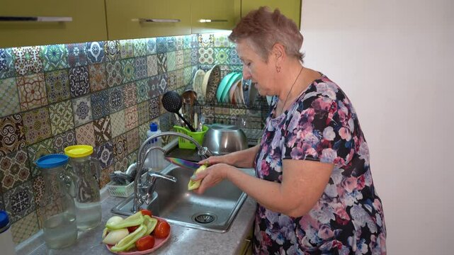 An elderly woman cuts and washes pepper and prepares a salad at home in the kitchen. Hands and knife close up. Wooden board. Food vegetables. Healthy eating
