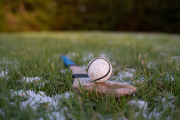 Hurling ball and stick lying on grass field in early morning snow. A close-up of hurling equipment...