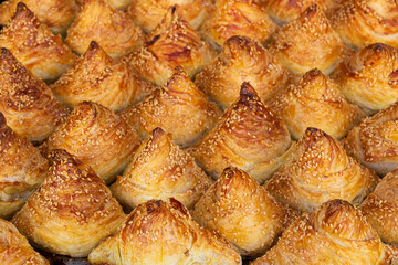 Background from freshly baked samsa with sesame seeds on sale at bazaar, Uzbekistan. Samosa is a popular savoury pastry in Central Asian cuisines. It represents a bun stuffed with meat or vegetables