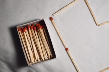 A box of matches sits beside a few loose ones, forming an intriguing composition on a subtle, light background.