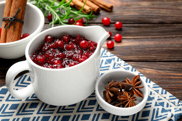 Tasty cranberry sauce in gravy boat and spices on wooden table, closeup