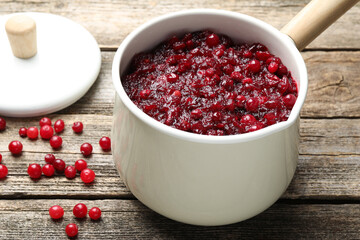Tasty cranberry sauce in saucepan and berries on wooden table, closeup