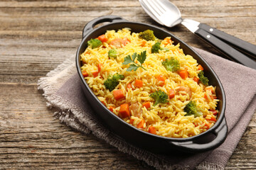 Tasty rice with vegetables in baking dish and cutlery on wooden table, closeup