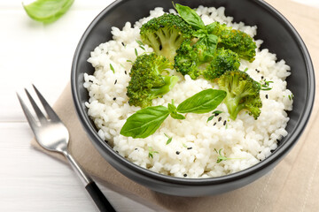Tasty rice with broccoli and basil on white wooden table, closeup