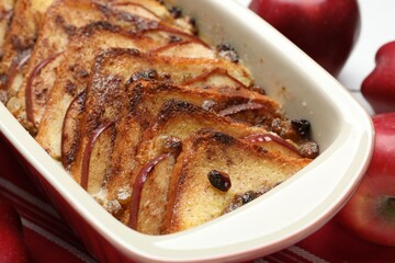 Delicious bread pudding in baking dish and fresh apples on table, closeup