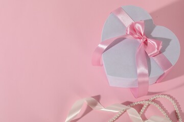 Beautiful wedding gift, ribbon and pearl jewelry on pink background, flat lay. Space for text