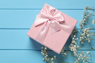 Beautiful wedding gift and gypsophila flowers on light blue wooden table, flat lay. Space for text