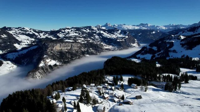 An enchanting aerial shot of the Swiss Alps in Stoos, where a sea of clouds gently rolls over the mountain peaks. A breathtaking winter view for nature lovers