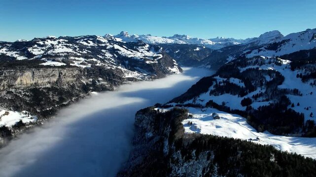 A stunning aerial view of Stoos, Switzerland, covered in snow. Thick fog blankets the valley, creating a breathtaking winter landscape in the Swiss Alps.