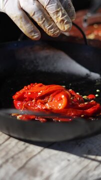 The chef arranges red pickled peppers in a pan, close up view