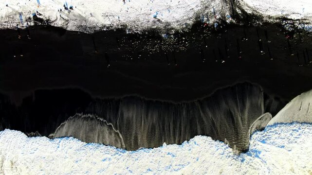 Aerial view of reynisfjara black sand beach with dramatic waves and snow, Vik, Iceland.
