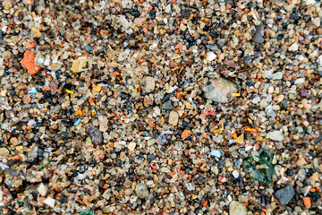 Close-up view of microplastic fragments scattered on beach, mixed with sand and pieces of glass, illustrating ocean and shore pollution, environmental impact