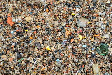 Close-up view of microplastic fragments scattered on beach, mixed with sand and pieces of glass,...