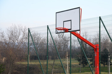 An outdoor basketball court with basketball backboard with orange hoop with chain net and with blue...