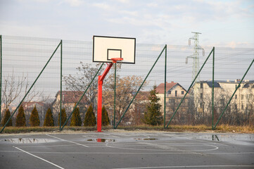 An outdoor basketball court with basketball backboard with orange hoop with chain net and with blue...