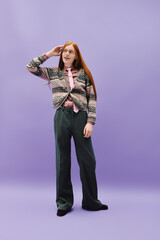 Dressed in a vibrant outfit, a young queer man strikes a playful pose in a pastel setting