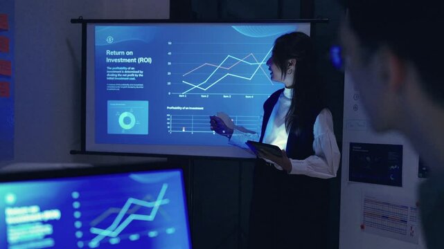 asian leader present business presentation in a dimly lit office, analyzing financial charts and data projections on a screen
