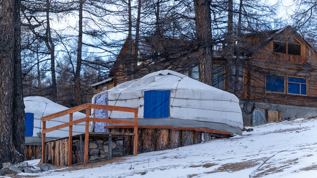 Traditional Mongolian Yurts in Snow - A winter scene in Khuvsgul, Mongolia, featuring traditional Mongolian yurts amidst snow-covered trees and rustic wooden structures.